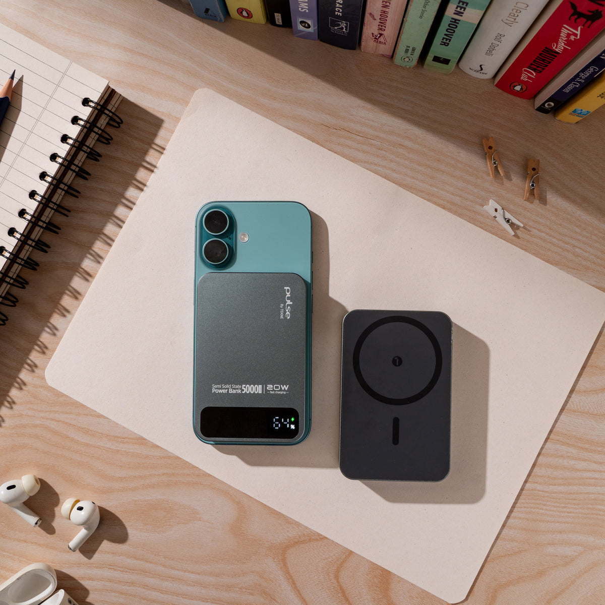 Teal Tekne power bank with dual camera cutout and digital display next to black wireless charging pad on desk with notebook