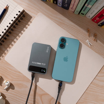 Blue iPhone and grey Tekne portable power bank charging on a wooden desk beside a spiral notebook